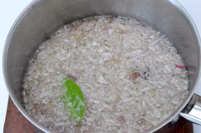 Star anise and bay leaf in pan of frying shallots.