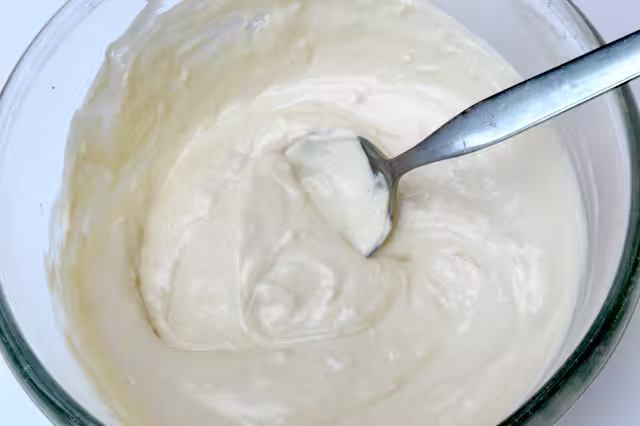 Yoghurt tahini sauce in mixing bowl with spoon.