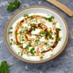 Bowl of tahini yoghurt sauce with wooden spoon above.