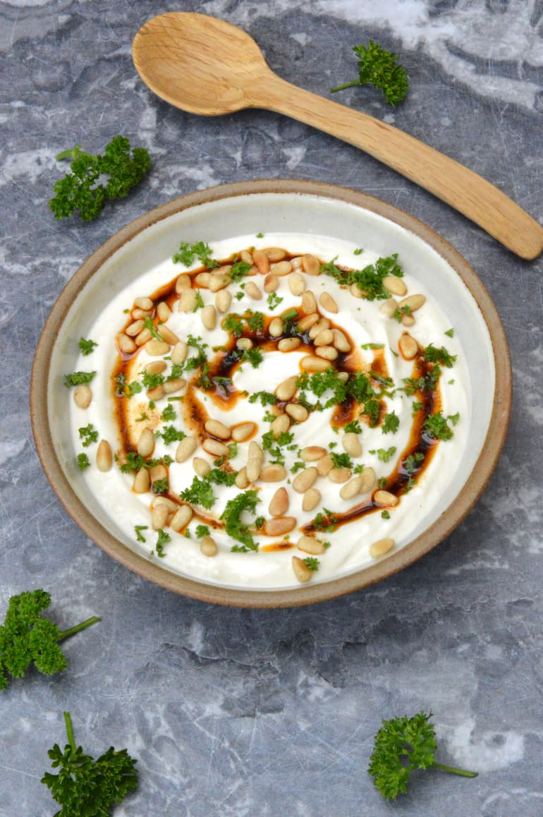 Bowl of tahini yoghurt sauce with wooden spoon above.