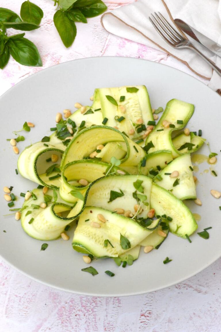 Ribbons of marinated courgettes curled on plate with herbs and toasted pine nuts.