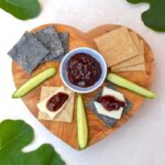 Crackers, cheese and homemade fig chutney on wooden board with fig leaves.