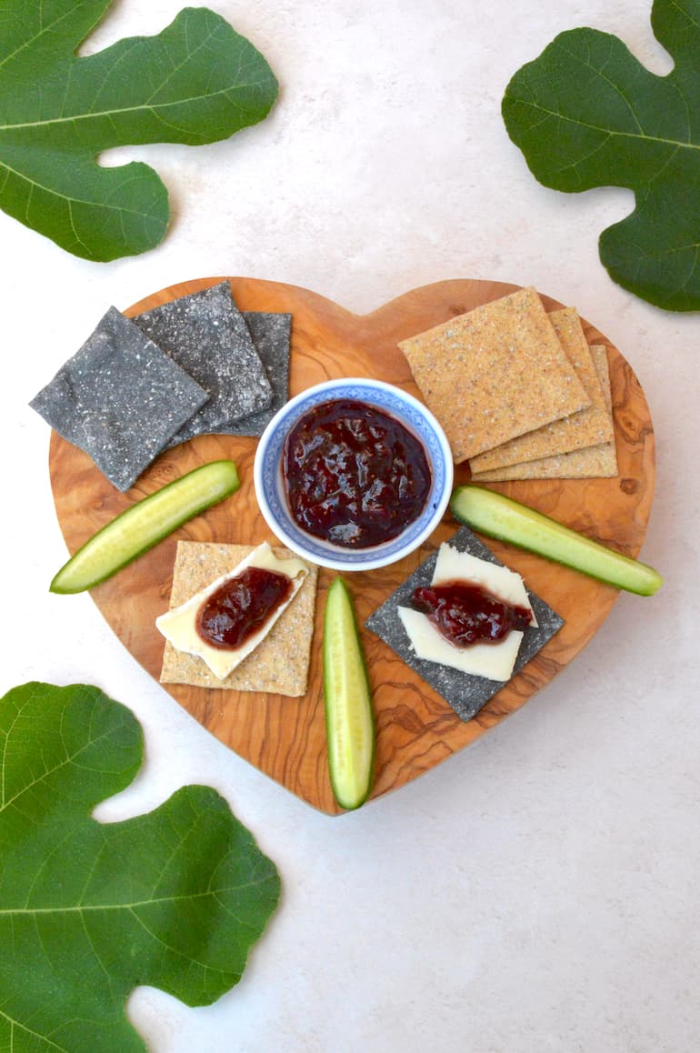 Crackers, cheese and homemade fig chutney on wooden board with fig leaves.