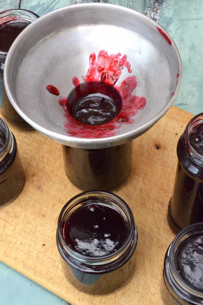 Homemade damson jam in jar with splattered jam funnel.