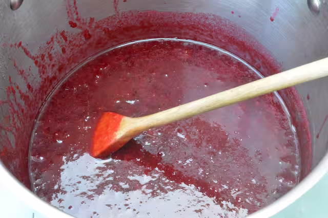 Stewed damsons, stirred in large saucepan with wooden spoon