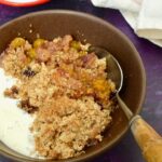 Bowl of ground cherry crumble with cream and spoon.