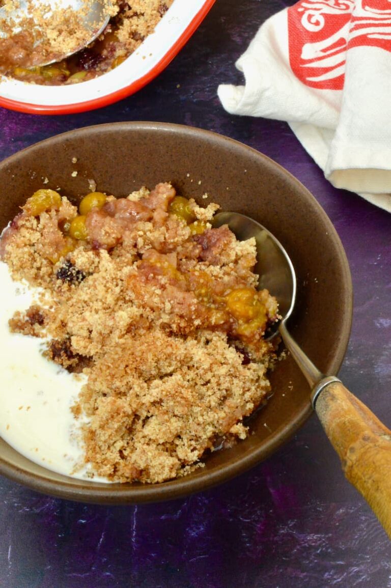 Bowl of ground cherry crumble with cream and spoon.