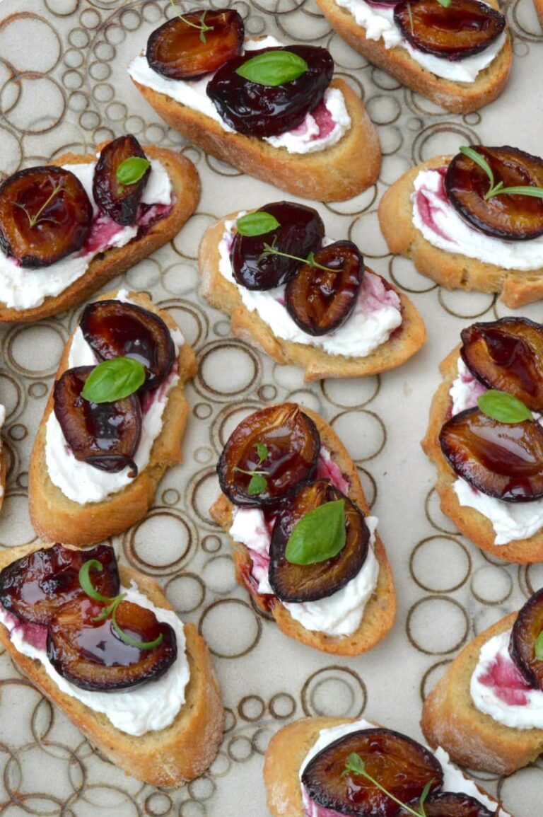 Platter of roasted plum bruschetta with whipped ricotta and herbs.