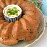 Partial view of pull apart savoury monkey bread with bowl of dip in its centre.