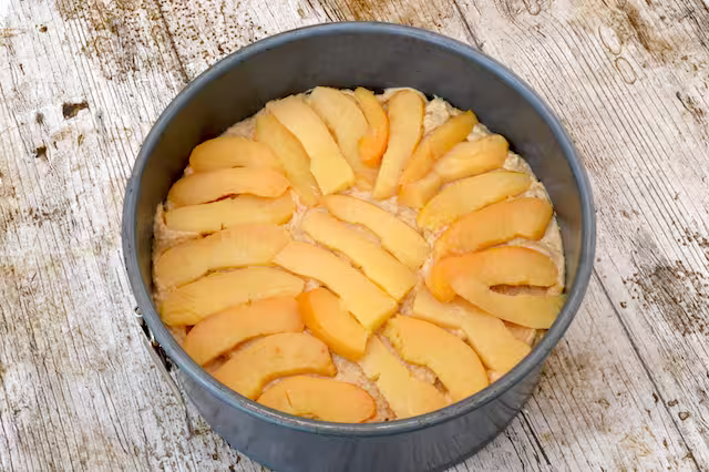 Poached fruit slices laid over batter in tin.