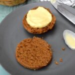 Two halves of a molasses scone on plate with one half spread with homemade lemon curd.