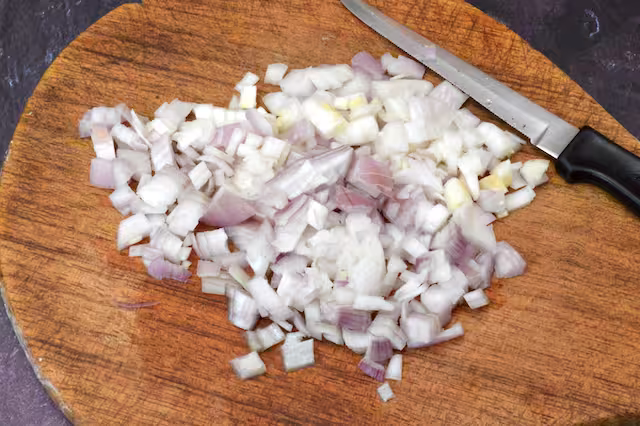 Diced shallot on chopping board with knife.