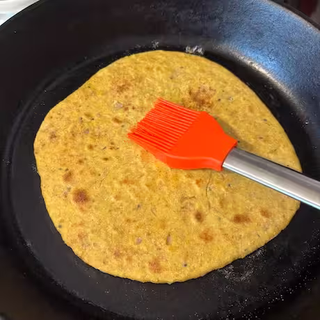 Brushing oil over baked paratha.