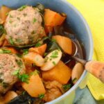 Partial view of swede and bean stew in a bowl with dumplings and spoon.