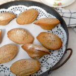 Homemade vegan madeleines on doily lined tray with cup of tea.