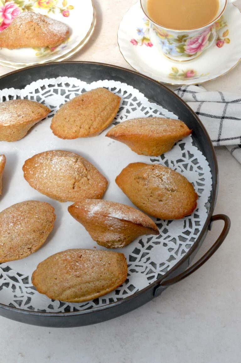 Homemade vegan madeleines on doily lined tray with cup of tea.