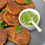 Vegan sweet potato tofu patties piled on plate with spoon inserted in bowl of green sauce.
