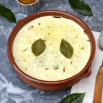 Baked dish of vegetarian lentil bobotie with two bay leaves on top and dish of chutney behind.