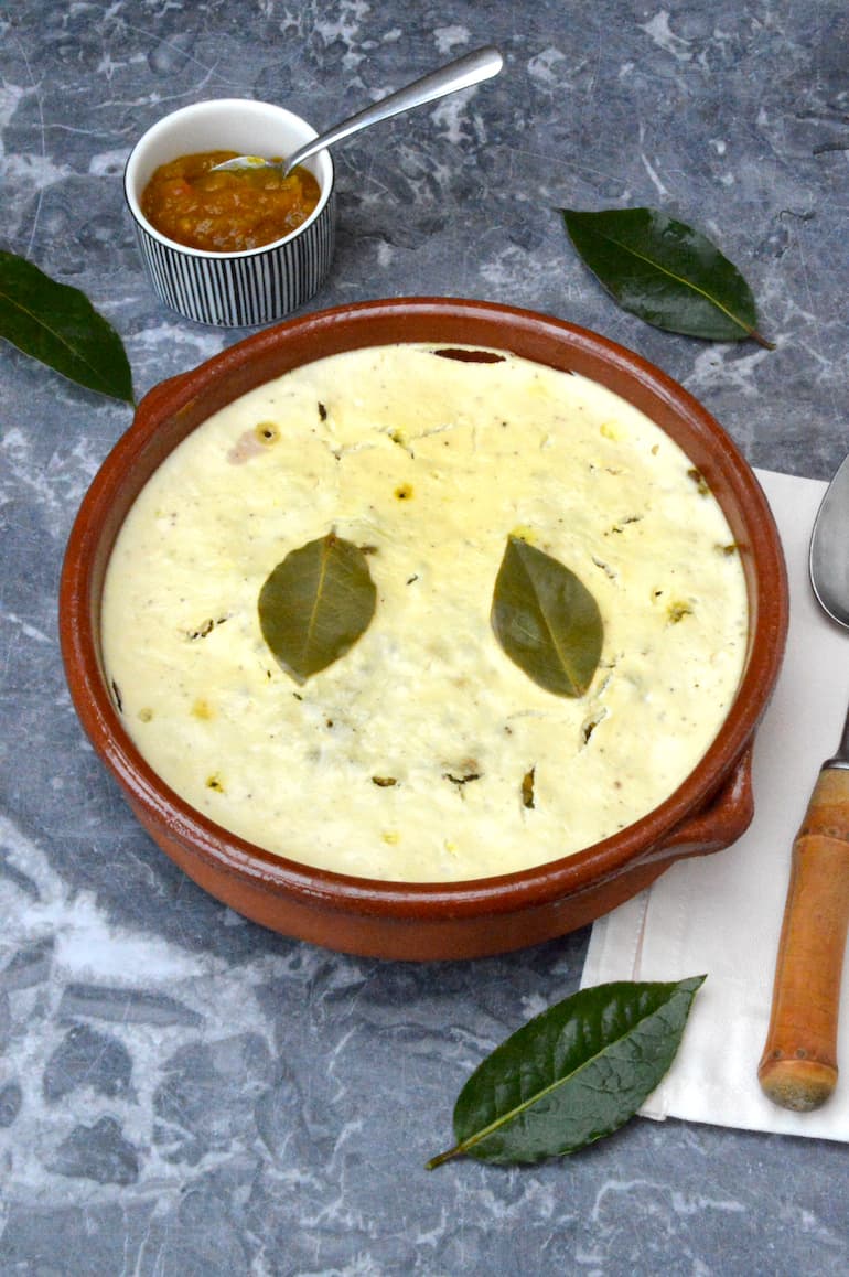 Baked dish of vegetarian lentil bobotie with two bay leaves on top and dish of chutney behind.