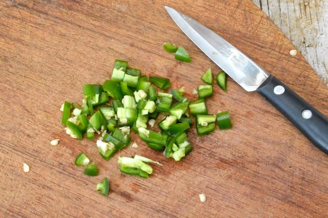 Chopped green chilli on cutting board with knife.