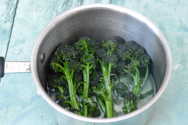 Boiled purple sprouting broccoli sitting in pan with water.