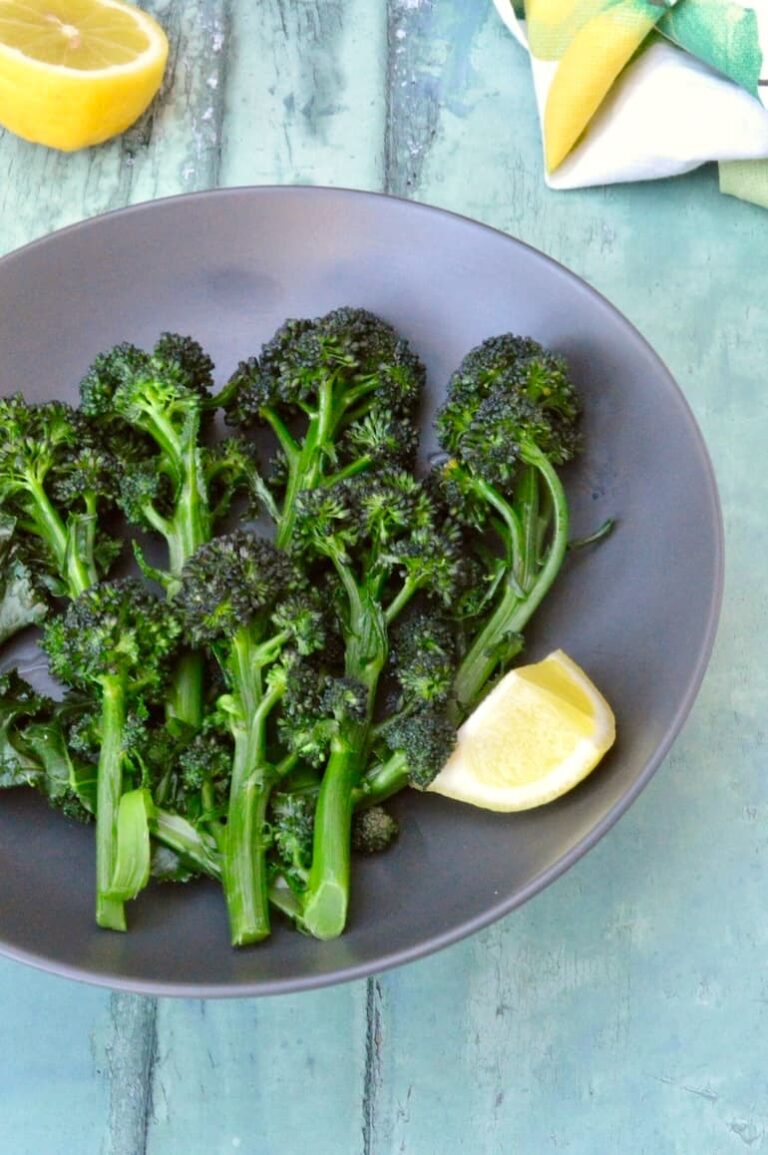Bowl of lightly boiled purple sprouting broccoli with lemon wedge.