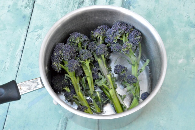 Purple sprouting broccoli in saucepan with stems in water and heads above.