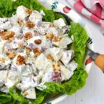 Bowl of Waldorf salad on bed of lettuce leaves with serving spoon.