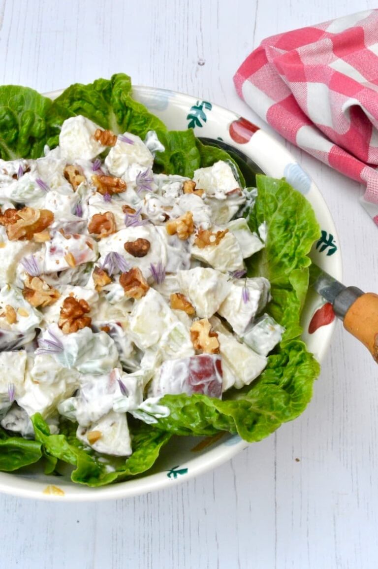 Bowl of Waldorf salad on bed of lettuce leaves with serving spoon.