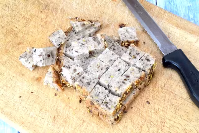 Seeded bread cubed on board with knife.