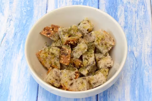 Seeded bread cubes in bowl with olive oil and oregano.