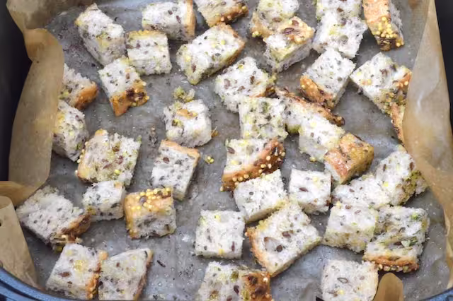Seeded bread cubes in lined air fryer basket.