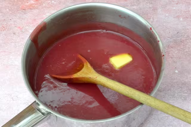 Cube of butter melting into hot raspberry curd.
