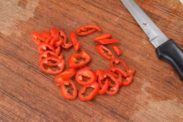 Deseeded red chilli sliced into rings on board with knife.