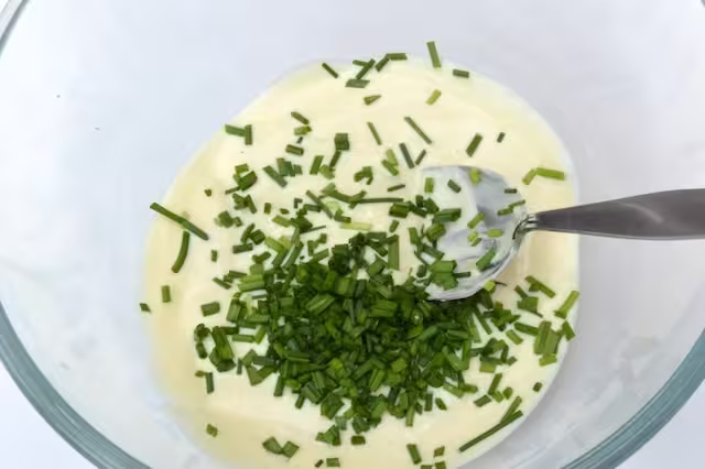 Snipped chives added to dressing in bowl.