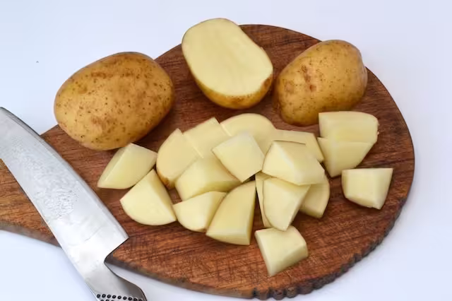 Cutting potatoes into chunks on a chopping board.
