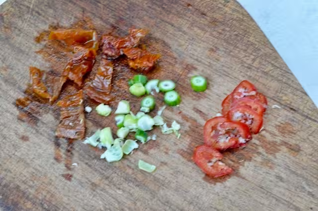 Chopped sun-dried tomatoes, garlic scapes and red chilli on board.