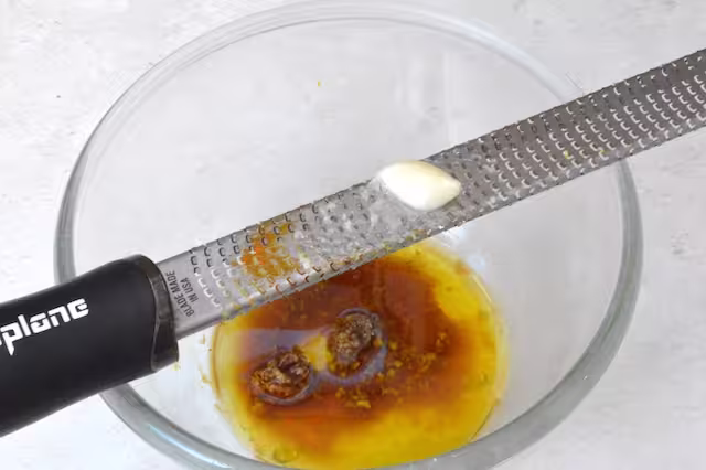 Grating garlic into dressing using microplane.