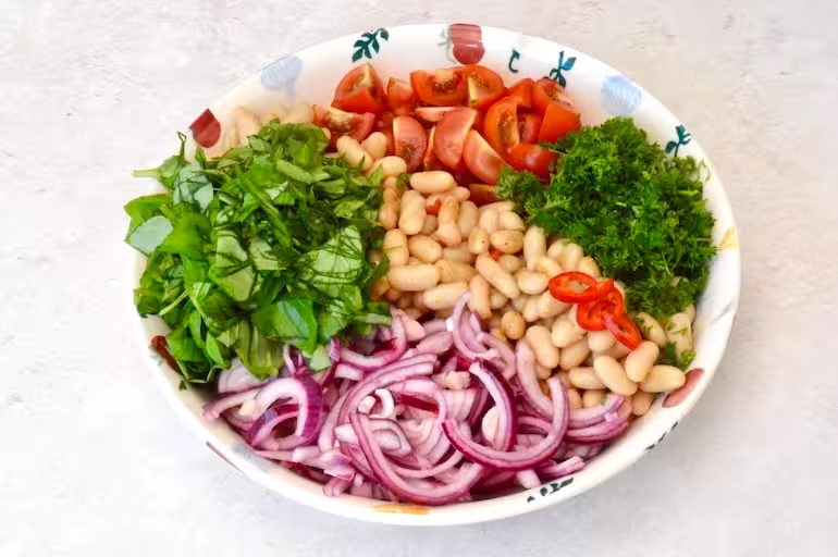 Italian bean salad ingredients laid out in serving bowl.