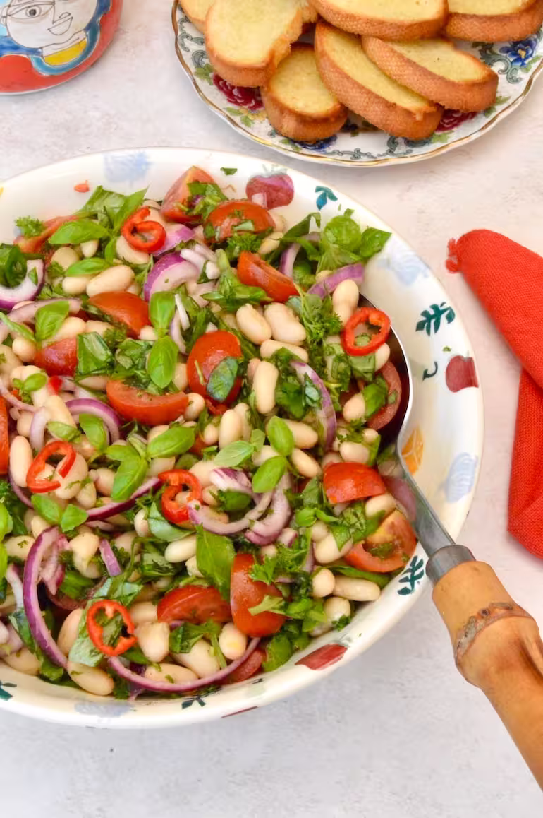 Bowl of Italian Tuscan bean salad with plate of crostini behind.