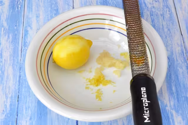 Zesting lemon into a bowl with grated garlic.