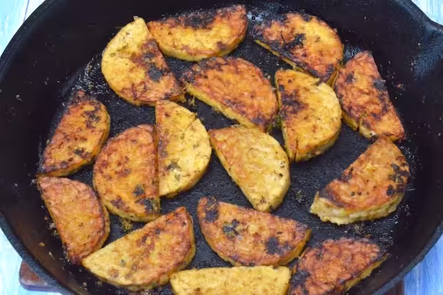 Flipped over tempeh slices frying in cast iron pan.