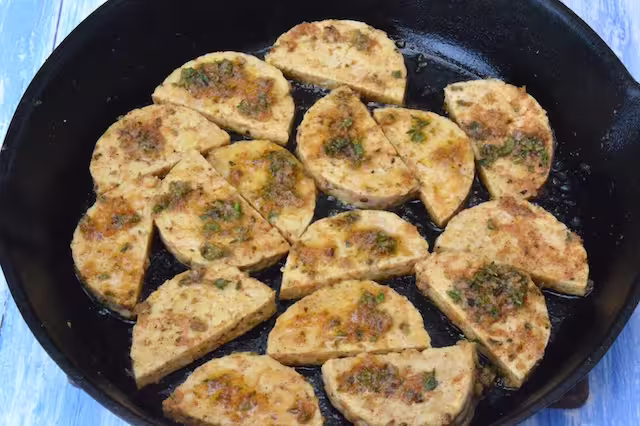 Tempeh slices in cast iron pan with remaining marinade on top.