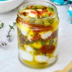 Jar of mozzarella balls marinading in olive oil and other ingredients.