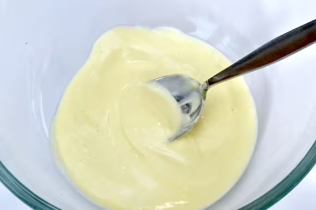 Mayonnaise, yoghurt and mustard stirred together in a glass mixing bowl.