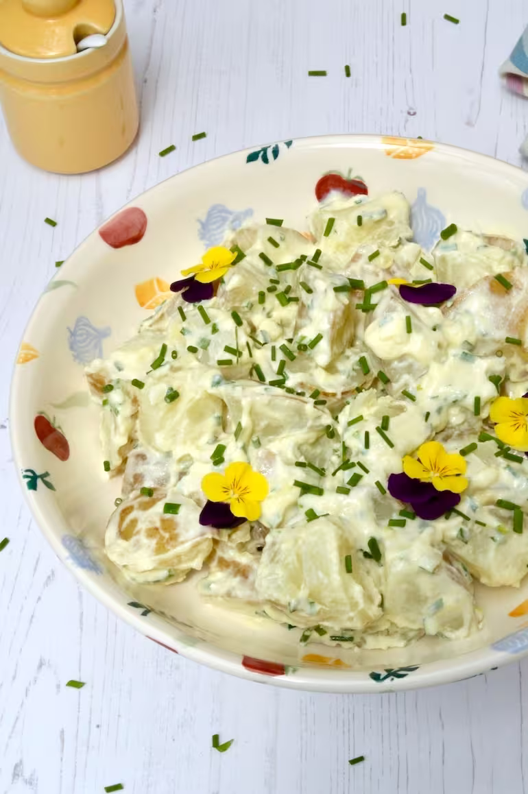 Bowl of simple creamy potato salad with chives and yellow pot behind.