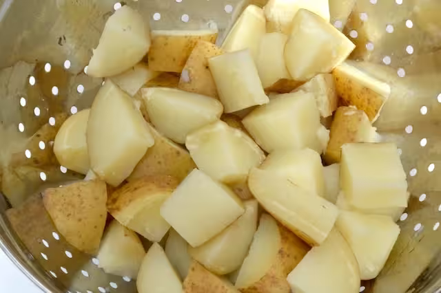 Boiled potatoes draining through a colander.