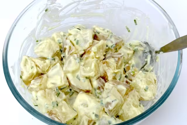 Bowl of cooked potatoes stirred into dressing.