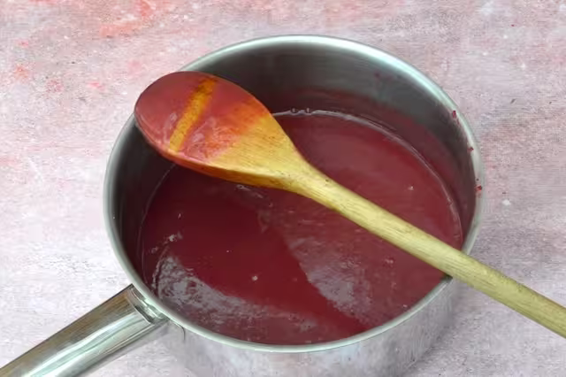Raspberry rose curd coating back of wooden spoon with trail remaining intact.