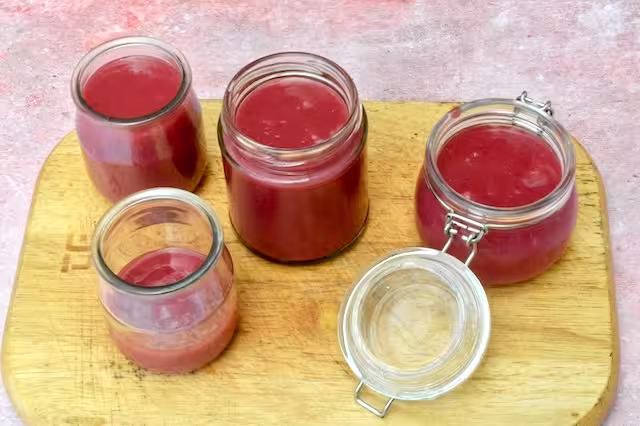 Three jars of raspberry rose curd with an extra one partially filled.